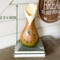 This shows the butterfly gourd vase that measures 12 by 6 inches.  The vase sits on a stack of books.